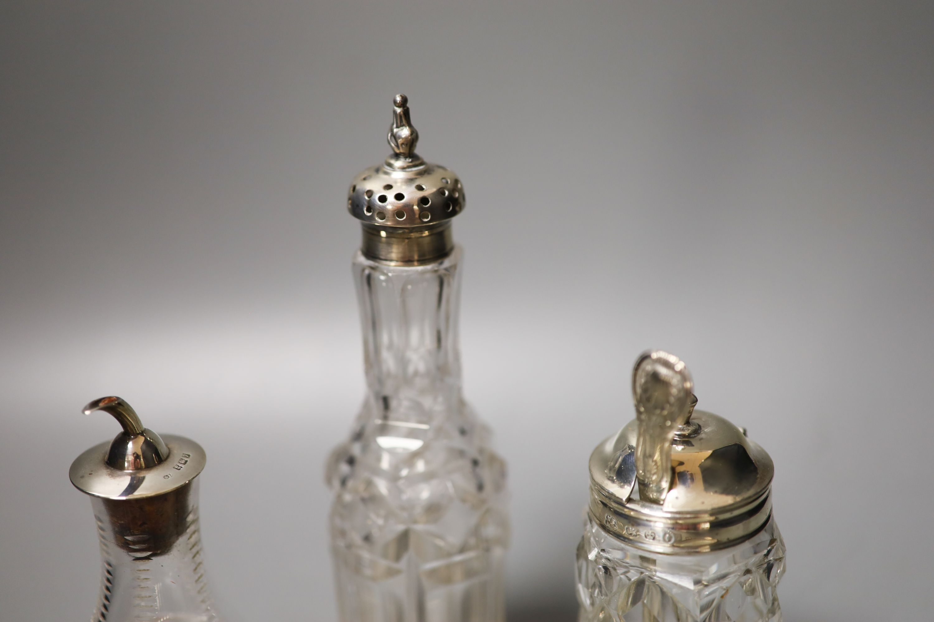 A pair of modern silver mounted glass butter dishes, a silver toastrack, three silver mounted glass bottles and three pairs of silver sugar tongs.